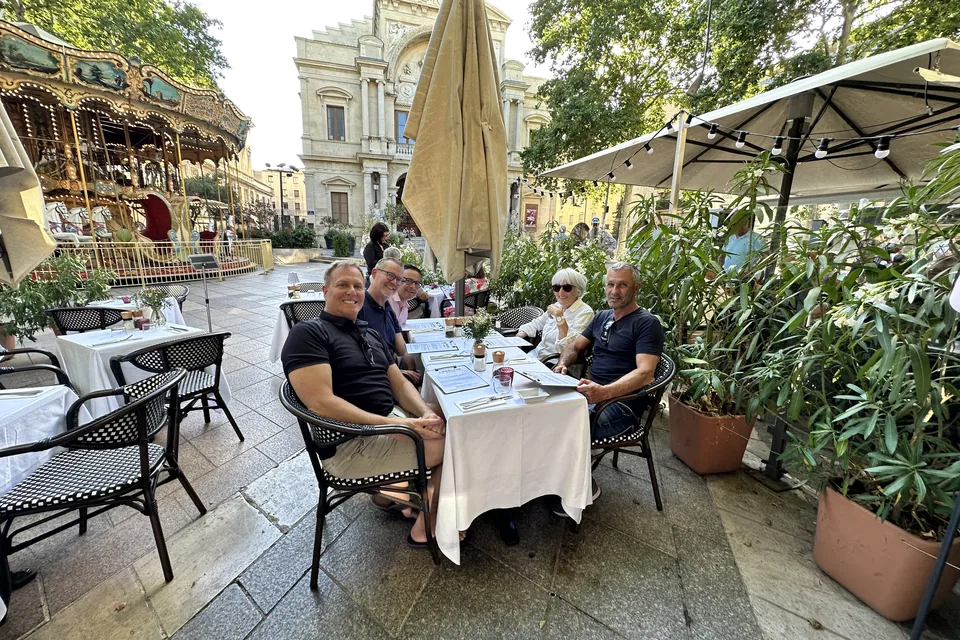 Friends at a café table on the Place de l'Horloge in Avignon, the carousel and the opera house behind.