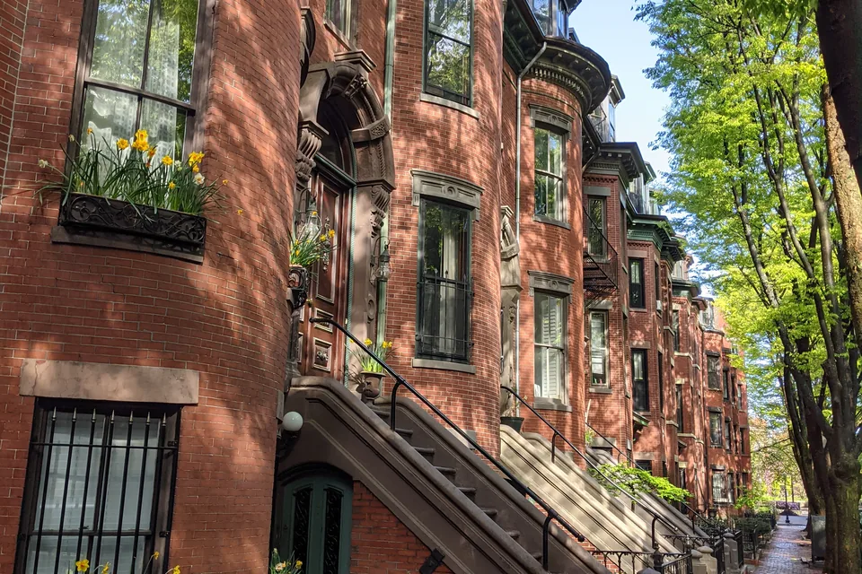 Curved brick bay fronts with daffodils in the window boxes along a tree-lined brick sidewalk in Boston.